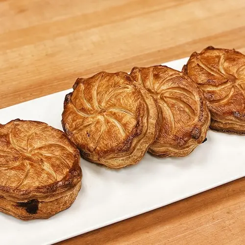 Four small buttery, flaky Galette de Rois arranged on a long white plate.