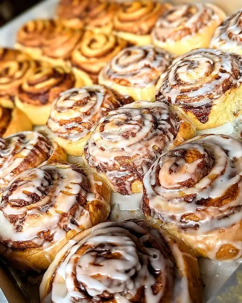 A tray of buttery rolls filled with spiced brown sugar swirl. Half are topped with a vanilla glaze.
