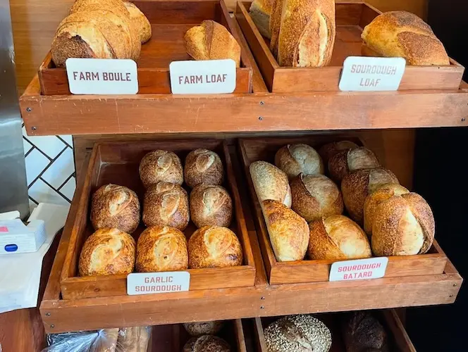 Bread shelf with farm boule, farm loaf, sourdough loaf, garlic sourdough, and sourdough batard.
